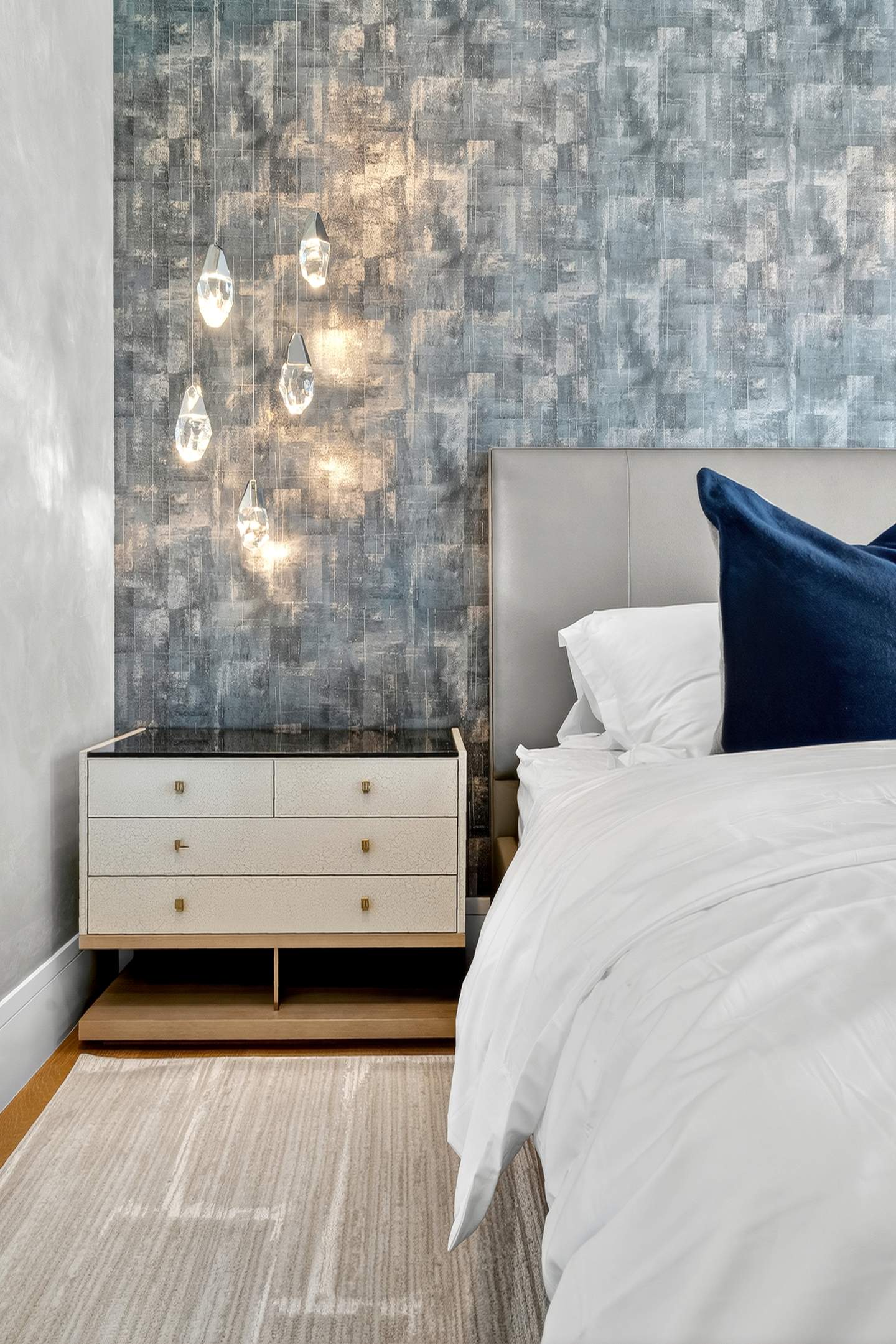 Second bedroom detail — crystal pendants, textured blue wallpaper, and navy pillow