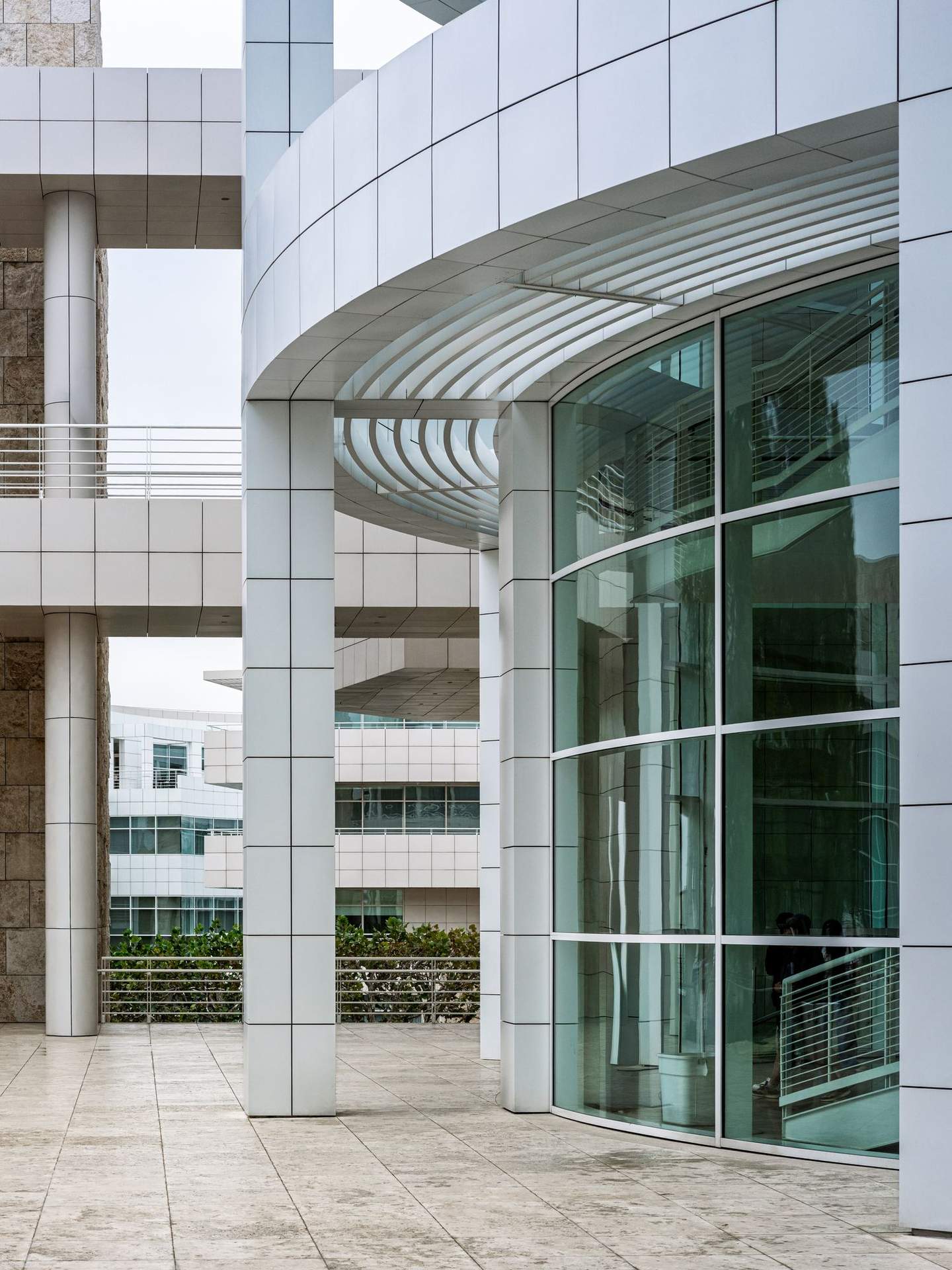 Getty Center glazed entry pavilion with curved curtain wall reflecting adjacent travertine structure, single figure providing scale