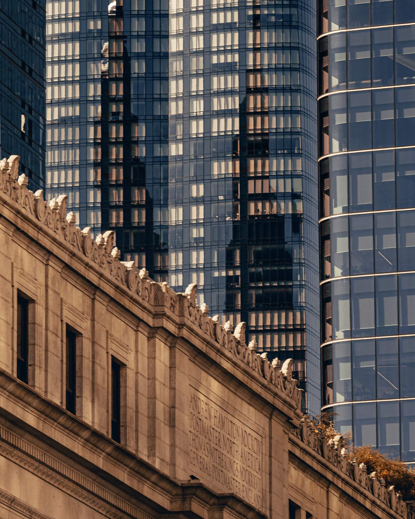 A Beaux-Arts civic building near Penn Station, Midtown Manhattan - early twentieth century. Detail of the carved limestone cornice frieze, with glass curtain wall towers rising behind