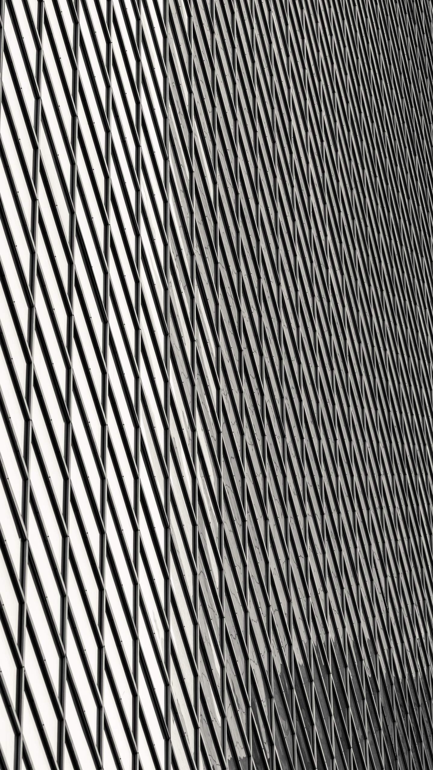 A facade system of overlapping rhomboid panels creating a continuous diagonal grid across a curved building surface, curvature causing the pattern to compress and shift subtly across the frame