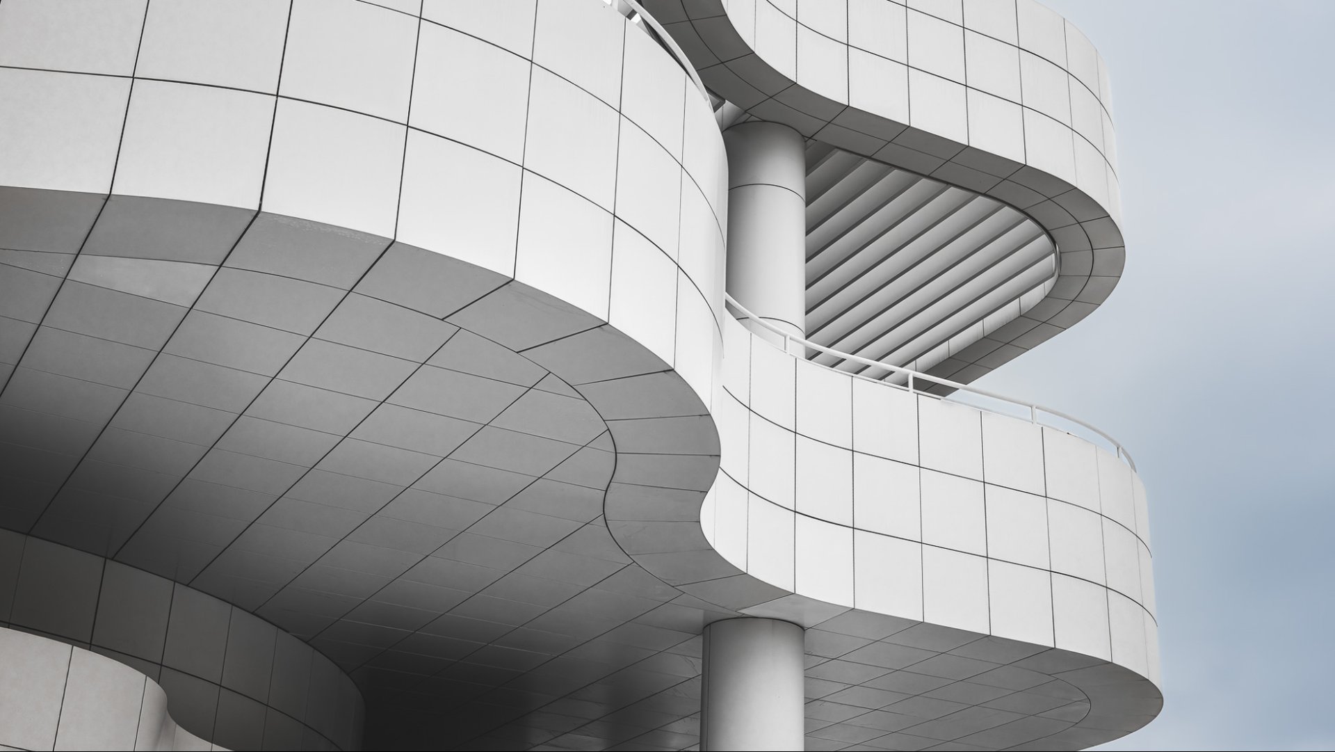 Curved white architectural facade with layered balconies photographed against a soft grey sky