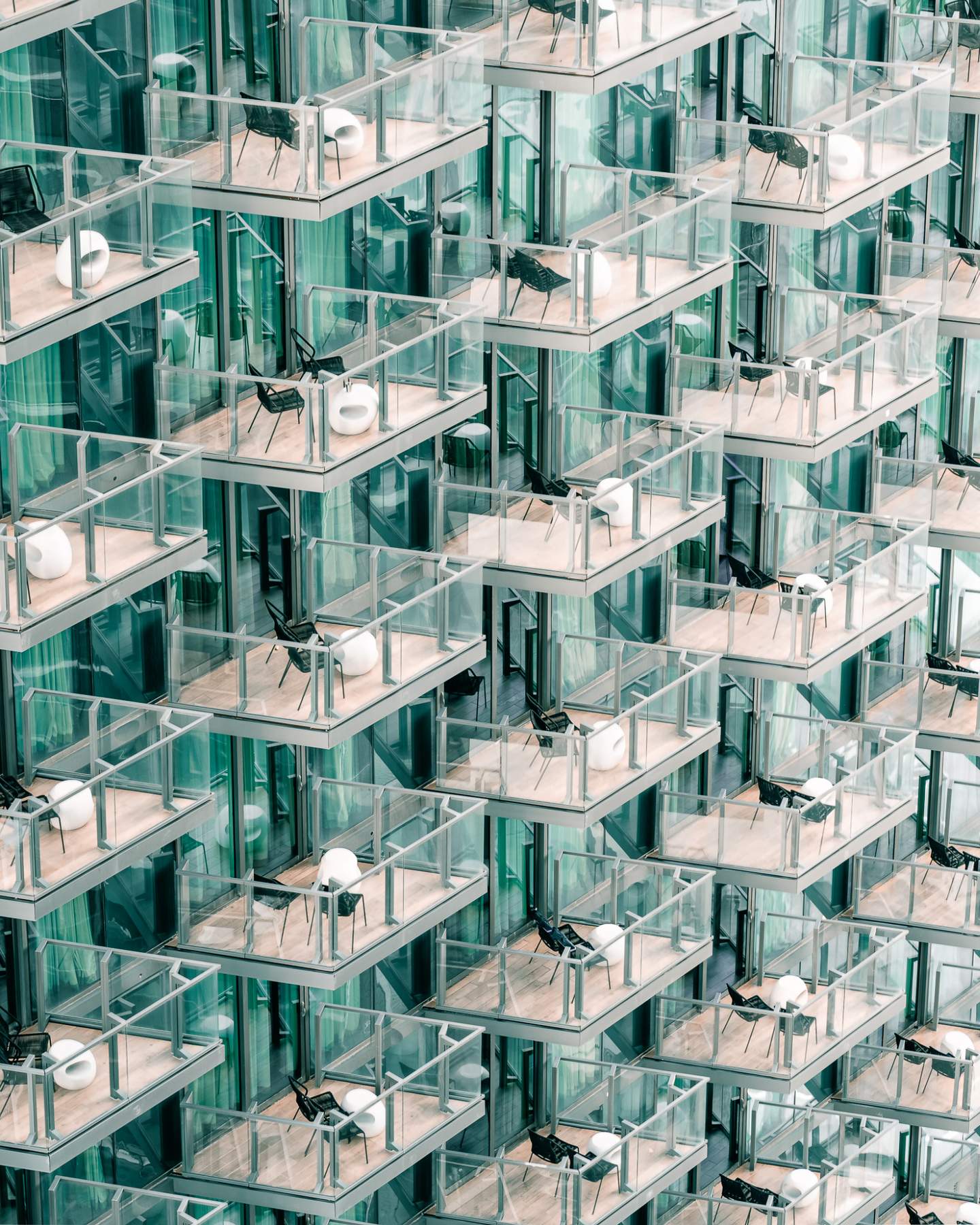 Repeating grid of stacked glass balconies on a luxury residential tower — architectural detail photography of a teal-tinted high-rise façade