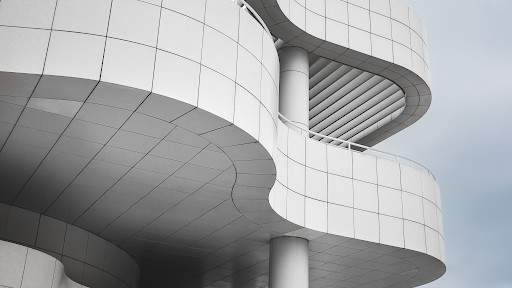 Curved white architectural facade with layered balconies photographed against a soft grey sky